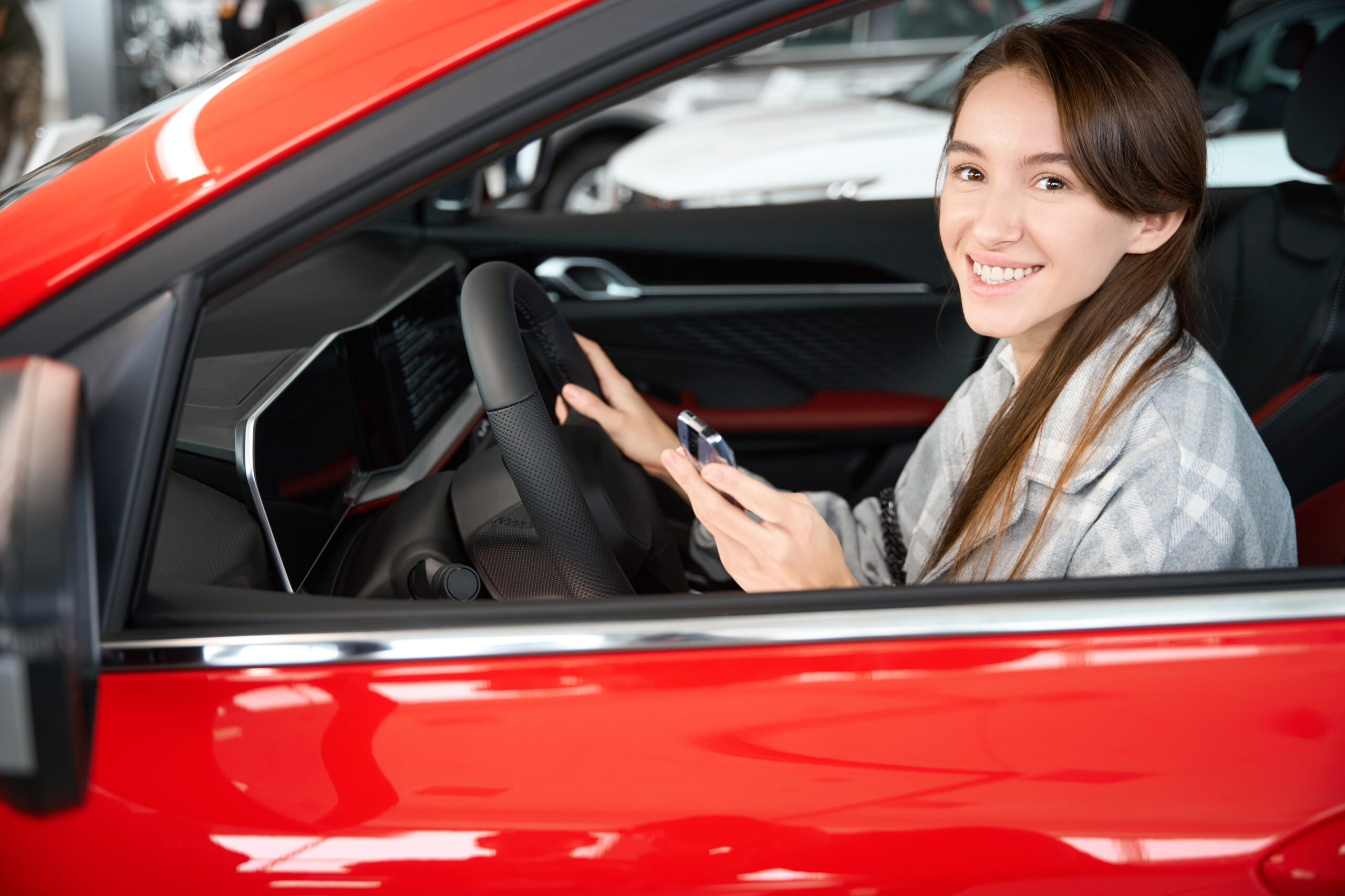 Happy young smiling woman sitting in new automobile enjoying her purchase in dealership