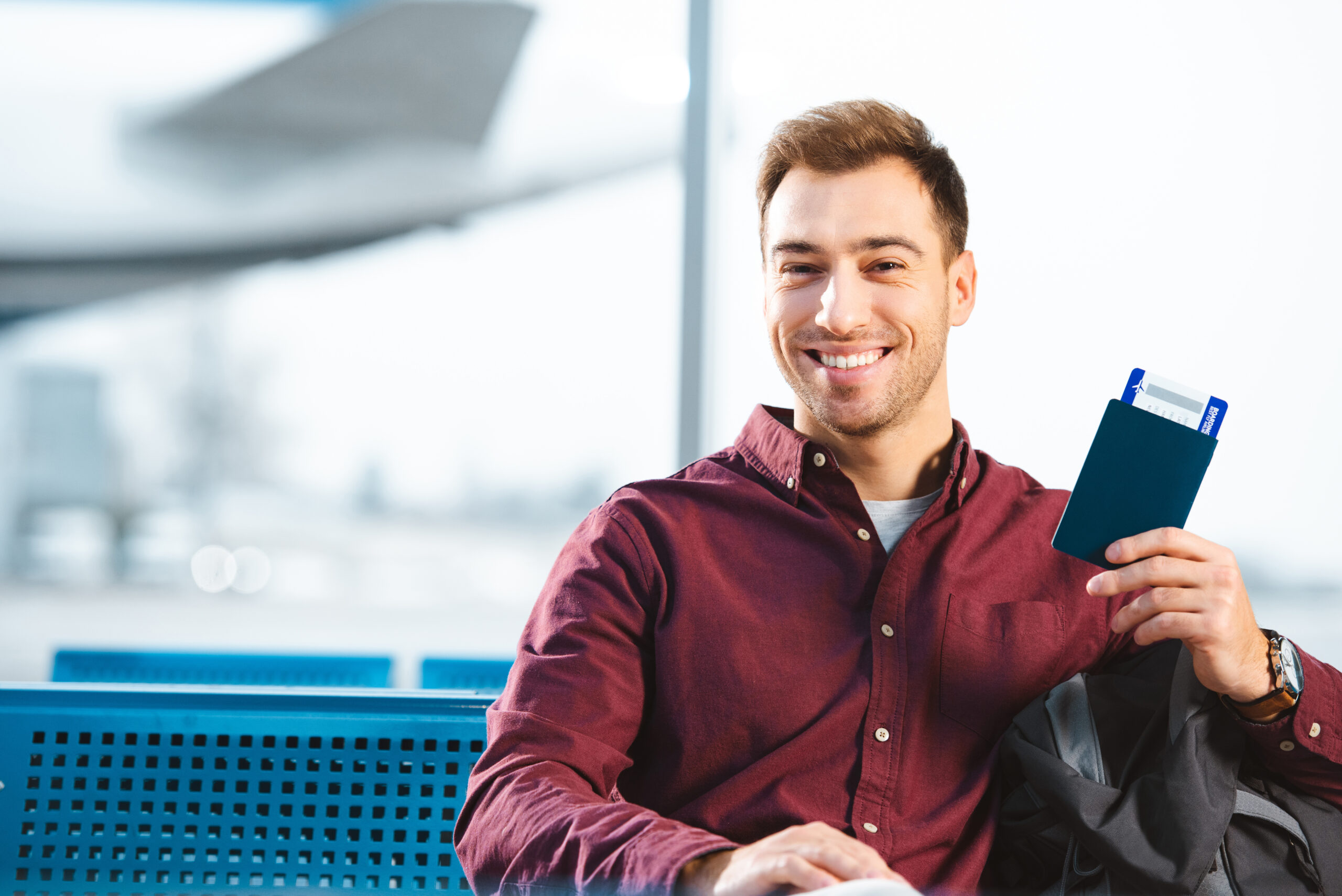 cheerful man holding passport with air ticket in waiting hall of airport