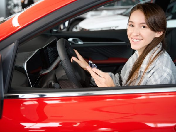 Happy young smiling woman sitting in new automobile enjoying her purchase in dealership